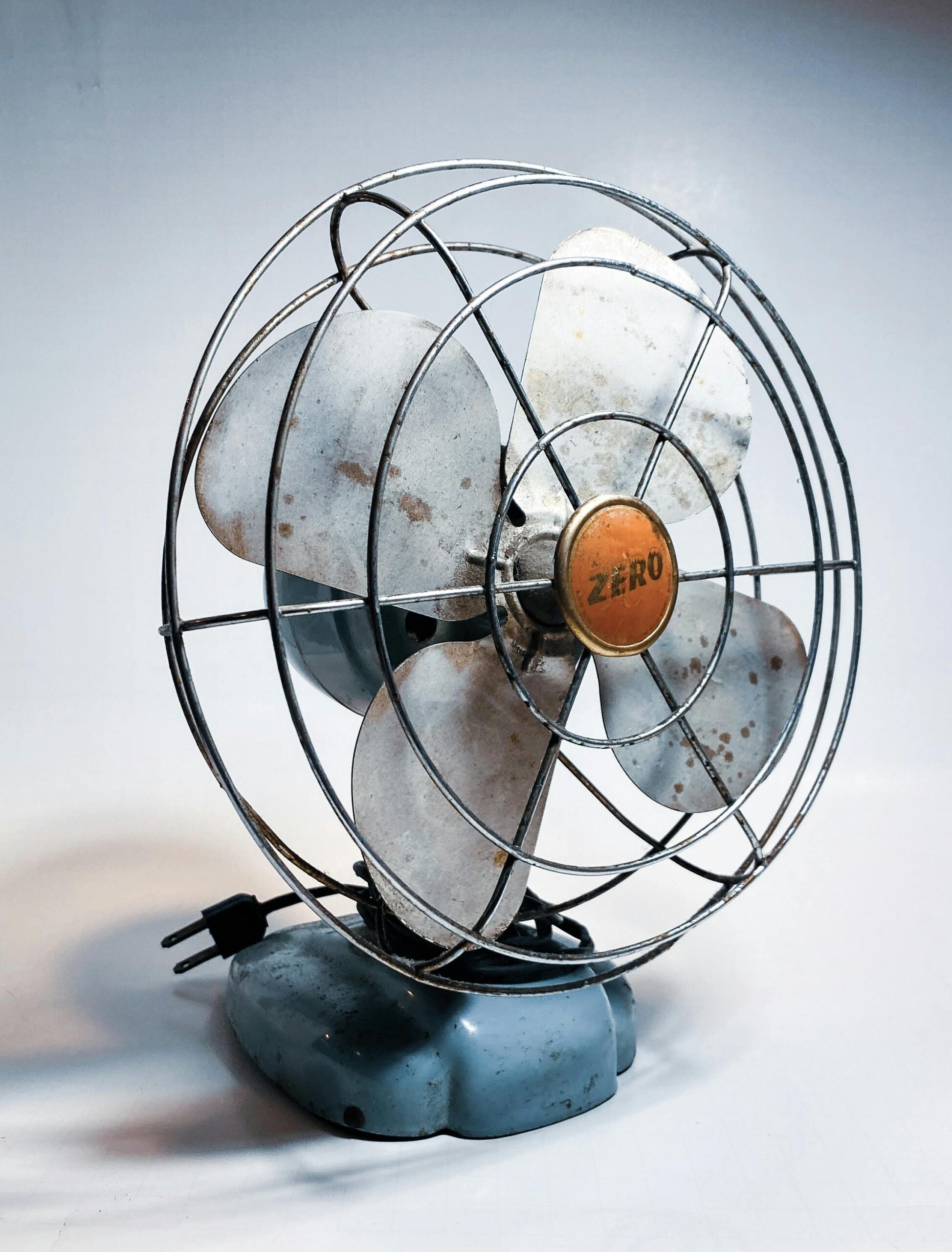 Close-up of a rustic vintage metal electric fan with a wire cage and plug, showcasing industrial charm.